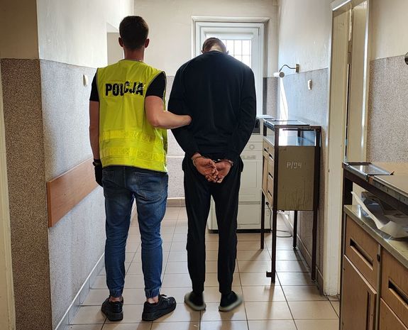 Policjant prowadzi zatrzymanego po korytarzu w budynku komendy.