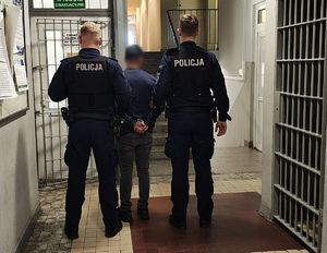 Policjanci prowadzą zatrzymanego po korytarzu w budynku komendy.