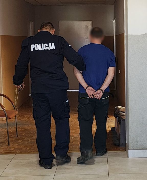 Policjant prowadzi zatrzymanego po korytarzu w budynku komendy.