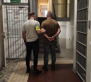 Policjant prowadzi zatrzymanego po korytarzu w budynku komendy.