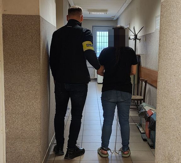 Policjant prowadzi zatrzymaną po korytarzu w budynku komendy.