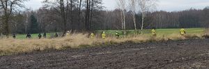 Policjanci i strażacy idą przez pola sprawdzając teren.