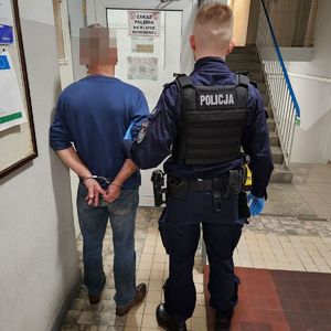 Policjant prowadzi zatrzymanego po korytarzu w budynku komendy.