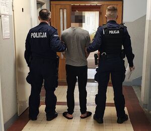 Policjanci prowadzą zatrzymanego po korytarzu w budynku komendy.