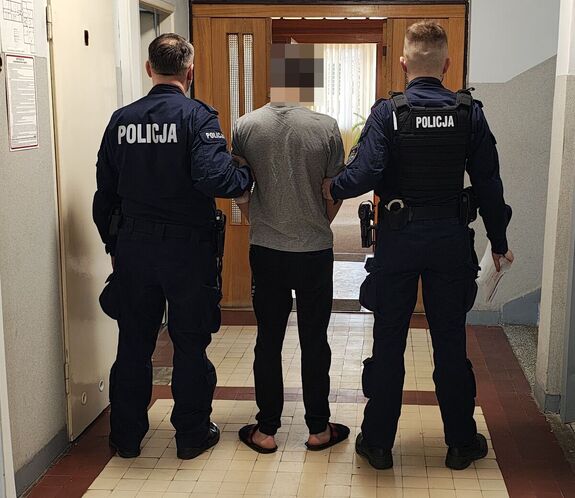 Policjanci prowadzą zatrzymanego po korytarzu w budynku komendy.