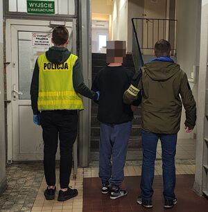 Policjanci prowadzą zatrzymanego po korytarzu w budynku komendy.