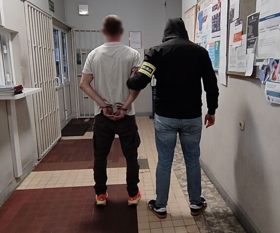 Policjant prowadzi zatrzymanego po korytarzu w budynku komendy.