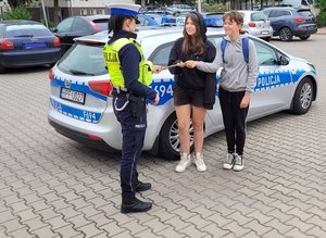 policjantka wręcza odblaski pieszym w tle radiowóz.