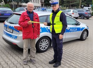 policjant wręcza element odblaskowy mężczyźnie na tle radiowozu.