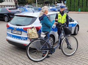 policjantka wręcza odblask rowerzystce na tle radiowozu.