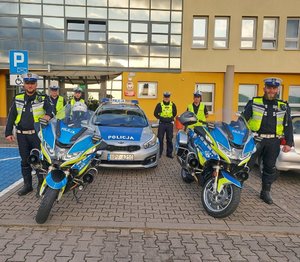 umundurowani policjanci przed Komendą Powiatową Policji w Wieruszowie w tle radiowóz i motocykle policyjne.