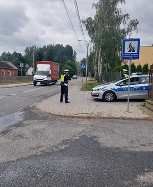 policjant mierzy prędkość pojazdom, obok zaparkowany radiowóz.