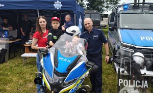 widzimy chłopca siedzącego na motocyklu na tle policyjnego namiotu wraz z policjantem i kobietą.