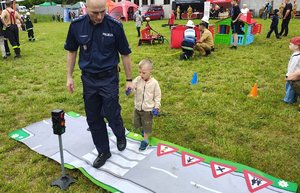 widzimy chłopca prowadzonego przez policjanta po dywanie miasteczka ruchu drogowego.
