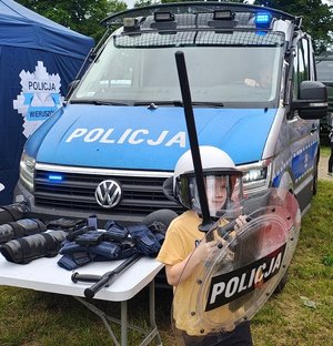 widzimy chłopca ubranego w specjalistyczny sprzęt na tle radiowozu.
