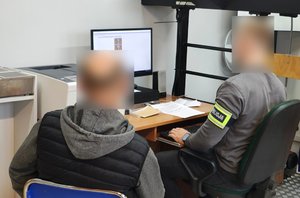 widzimy policjanta siedzącego przed komputerem i osobę zatrzymaną.