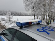 na zdjęciu widoczna część radiowozu policyjnego , w tle zimowa aura, łąka i las pokryty śniegiem