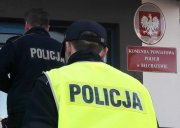 umundurowani policjanci wchodzący do komendy policji. Widoczni tyłem, w tle wejście do budynku komendy, oraz tabliczka koloru czerwonego  z napisem Komenda Powiatowa Policji w Bełchatowie.