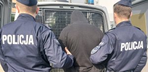 policjanci prowadzą zatrzymanego mężczyznę. w tle radiowóz policyjny