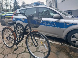 rower za nim widoczne radiowozy policyjne. zdjęcie zrobione na placu wewnętrznym komendy