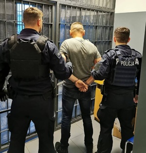 zatrzymany mężczyzna. policjanci prowadzą sprawce przestępstwa. zdjęcie zrobione w pomieszczeniu służbowym