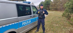 umundurowany policjant stoi przy radiowozie, teren parku
