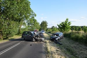 miejsce zdarzenia, dwa rozbite pojazdy po zderzeniu czołowym, jeden stoi na drodze, drugi rozbity w rowie, na miejscu służby ratunkowe, policja i straż.