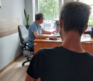 pomieszczenie służbowe policji, przy biurku policjant  który pisze przy komputerze, obok na krzesełku siedzi mężczyzna, który jest przesłuchiwany przez policjanta.