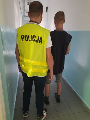 Funkcjonariusz w kamizelce odblaskowej z napisem Policja stoi obok zatrzymanego mężczyzny