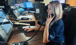 policjantka na stanowisku dowodzenie komendy policji w czasie służby, siedzi przy biurku przed komputerem, rozmawia przez telefon.