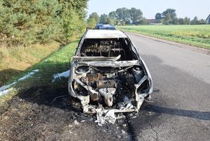 widok uszkodzonego auta, po pożarze. auto stoi przy drodze.