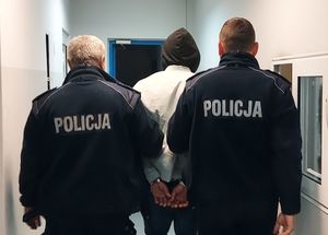 policjanci prowadzą zatrzymanego. zdjęcie zrobione na korytarzu komendy.