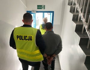 policjanci prowadzą zatrzymanego mężczyznę. zdjęcie zrobione na klatce schodowej komendy.
