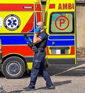 policjant, w tle karetka pogotowia ratunkowego.