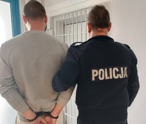 policjant prowadzi zatrzymanego mężczyznę, zdjęcie zrobione w pomieszczeniu służbowym.