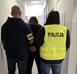 Dwóch funkcjonariuszy Policji z zatrzymanym mężczyzną.