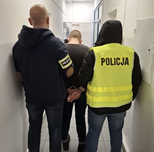 Dwóch funkcjonariuszy Policji z zatrzymanym mężczyzną.