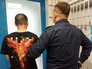 policjant prowadzi zatrzymanego mężczyznę, zdjęcie zrobione w pomieszczeniu służbowym.
