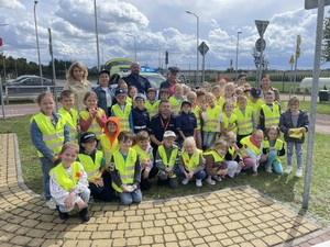 na zdjęciu policjanci z przedszkolakami oraz ich pedagogami, dzieci mają założone kamizelki odblaskowe. Zdjęci zrobione na placu miasteczka ruchu drogowego.