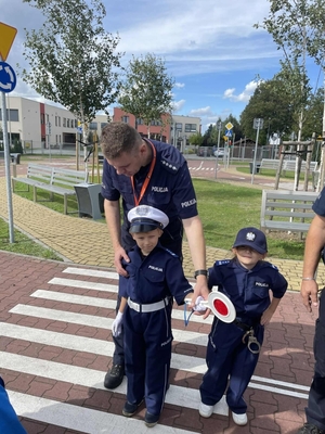policjant pokazuje chłopcom na czym polega praca policjanta ruchu drogowego w obrębie przejścia dl pieszych, policjanci uczą dzieci prawidłowych zachowań na przejściu dla pieszych.