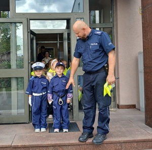 policjant razem z przedszkolakami. policjant wyprowadza dzieci z posterunku po zajęciach dotyczących bezpieczeństwa.