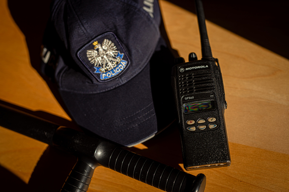 Czapka Policyjna z daszkiem, krótkofalówka oraz pałka typu tonfa.
