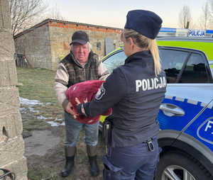 Policjantka przy radiowozie daje mężczyźnie koc.