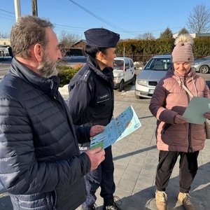 Policjantka rozmawia z seniorami i przekazuje ulotkę.