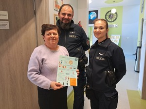 Policjanci z seniorką, która trzyma w ręku ulotkę.