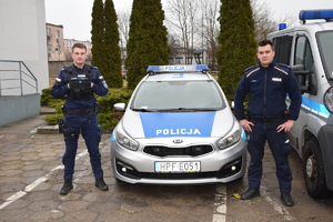 Dwóch policjantów stoi przy radiowozie.