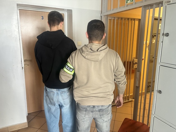 Policjant kryminalny prowadzi zatrzymanego mężczyznę.