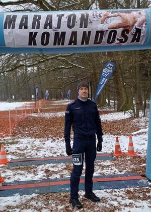 Umundurowany policjant, stojący na tle banneru maratonu.