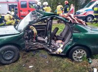 Miejsce zdarzenia drogowego w Dominikowicach.  Wrak rozbitego zielonego audi A4. W tle wóz strażacki i karetka pogotowia oraz pracujący ratownicy