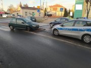 Miejsce zdarzenia drogowego w Poddębicach. Zielony peugeot 208 uderzył w znak drogowy. W tle oznakowany radiowóz policji, inne pojazdy, budynki, drzewa, krzewy i znaki drogowe.